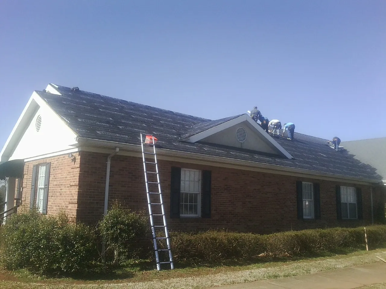 Crew tearing shingles off a brick ranch roof with a ladder set — Emergency Roof Repair work by our crew in Morehead