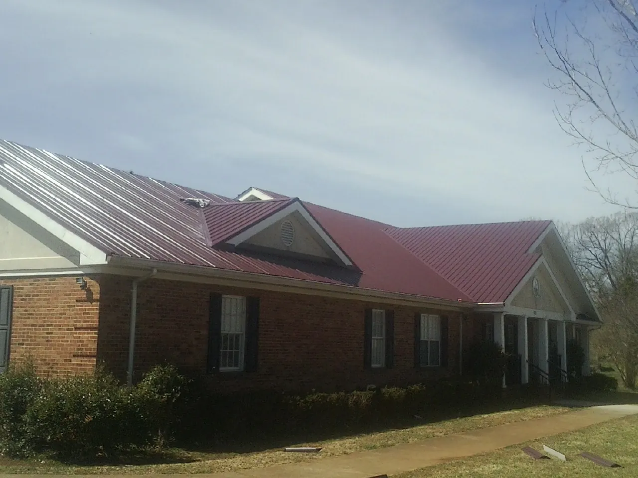 Red metal roof with gabled entries on a long brick building, from a Hail Damage Roof Repair job in Morehead