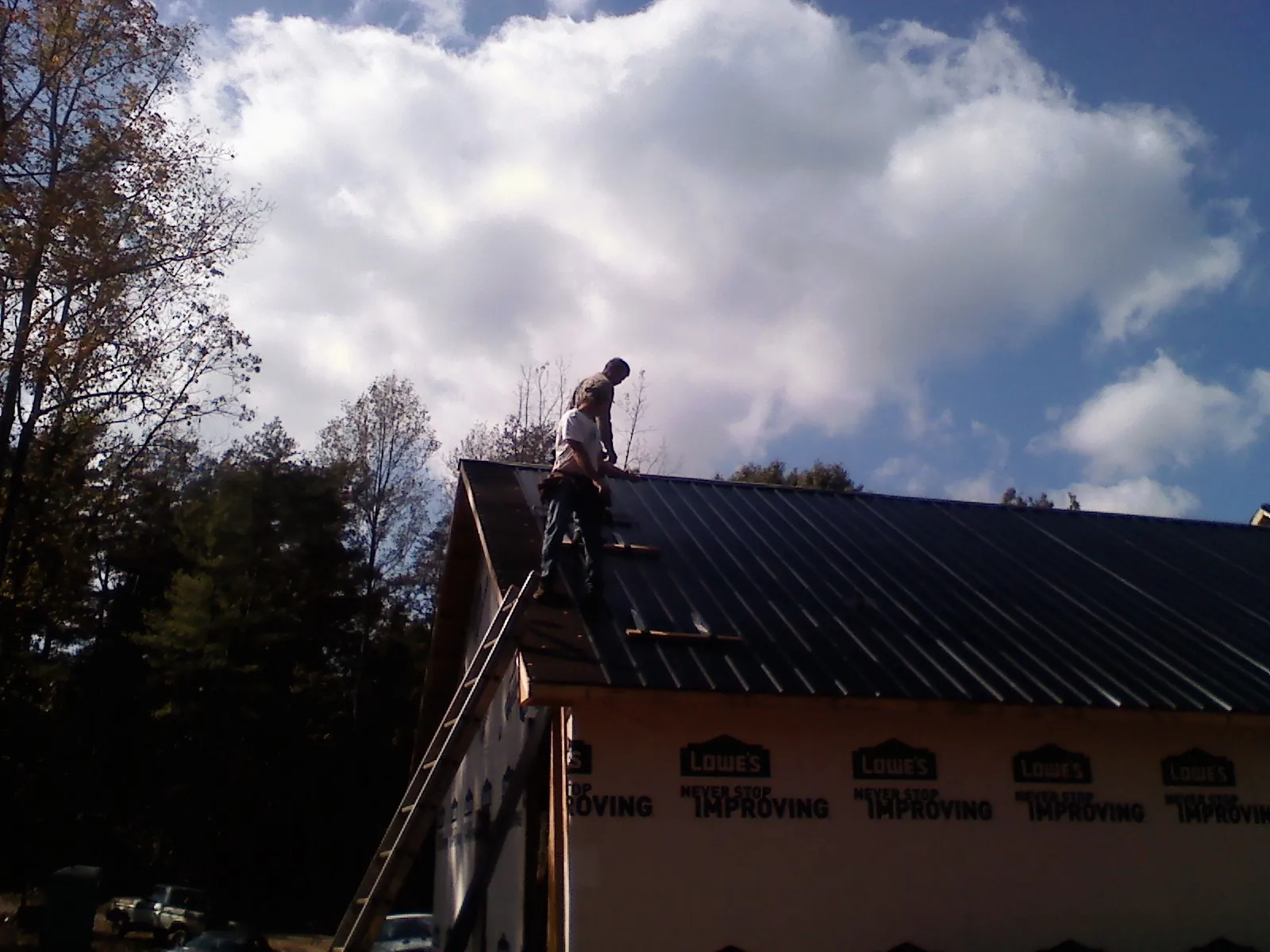 Roofer fastening dark metal panels high against a cloudy sky, from a Roof Inspection job in Morehead