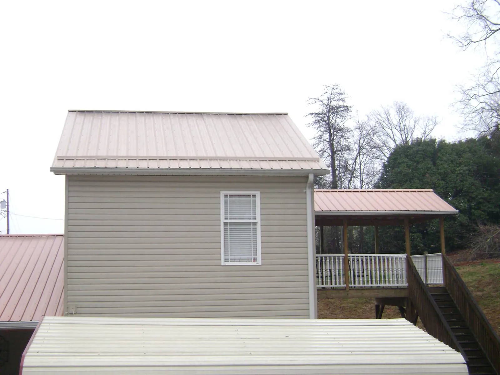 Tan metal roofs on a two story addition and attached porch, from a Roof Replacement job in Morehead